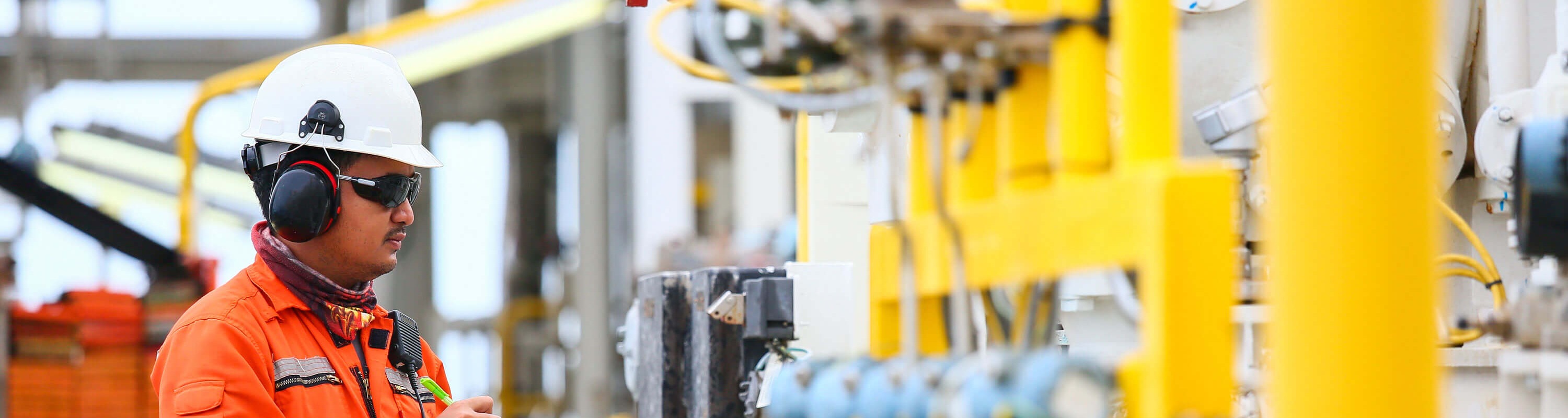 Rig worker in an orange high-vis jacket and white hard hat, reviewing the facility's water treatment equipment