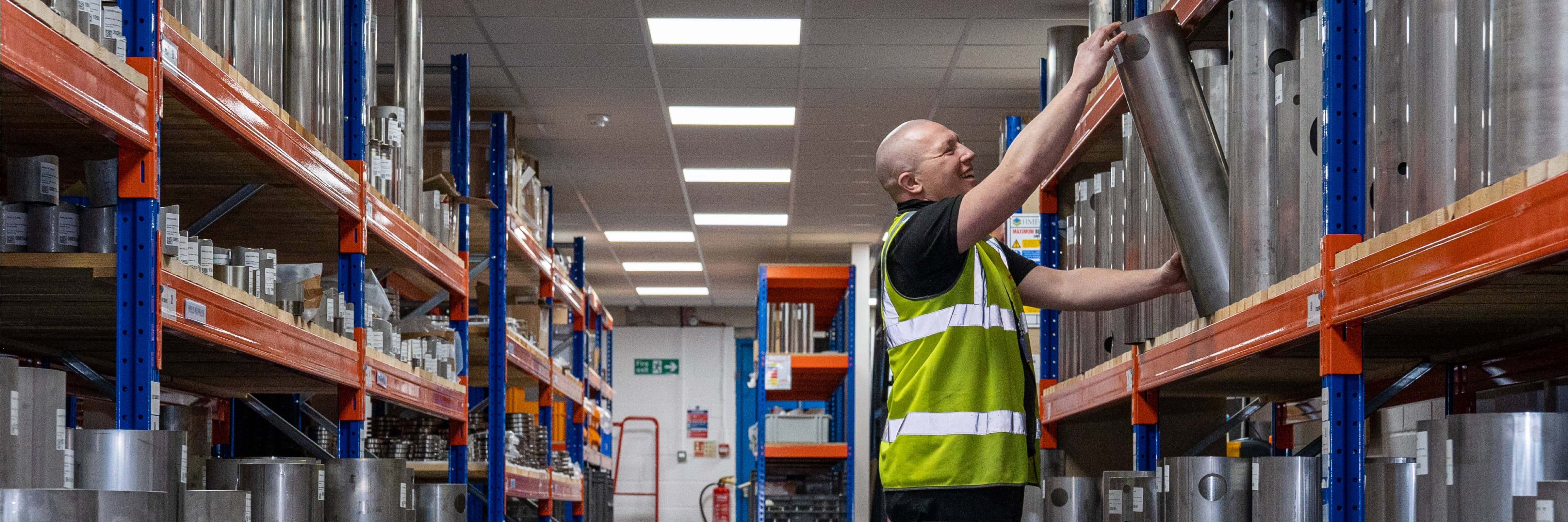 Factory worker in a high-vis jacket selecting a filter from a stacked shelf